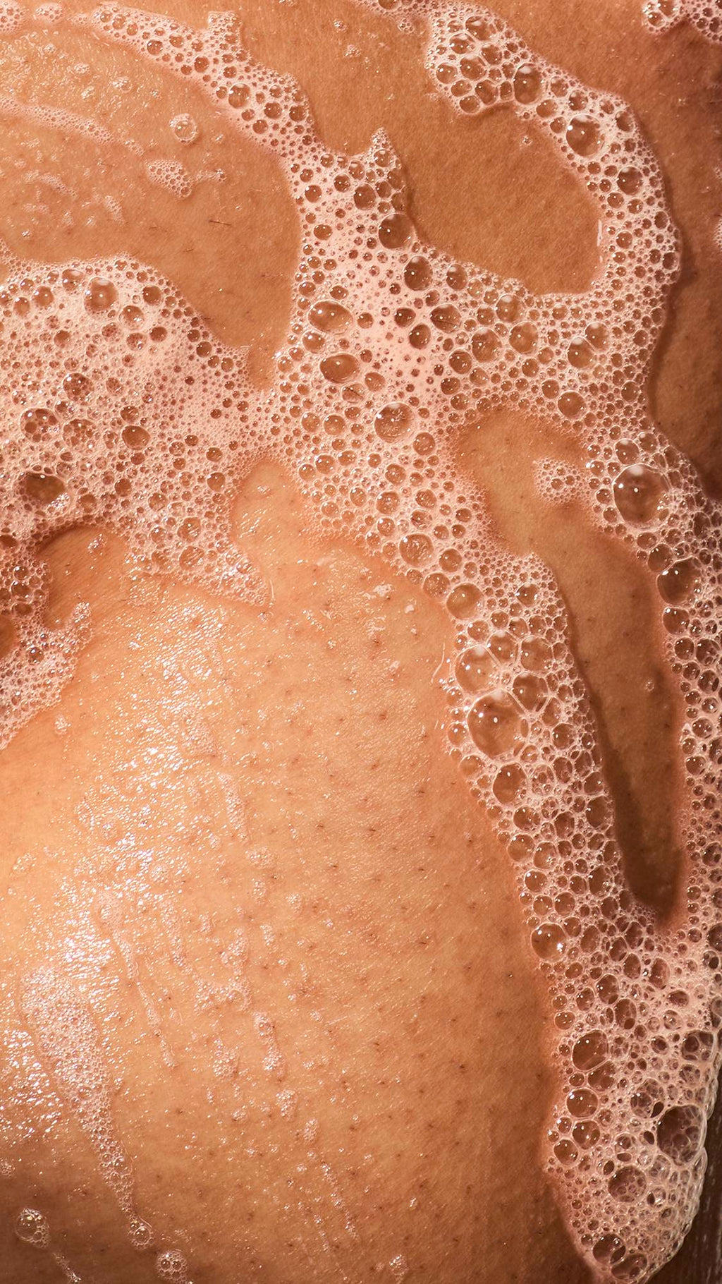 A close-up of wet skin covered in thick trails of soapy lather and clusters of small bubbles.